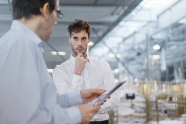 Young businessman looking at colleague in a factory - DIGF10705