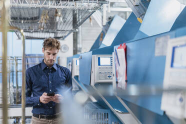 Young businessman using smartphone in a factory - DIGF10728