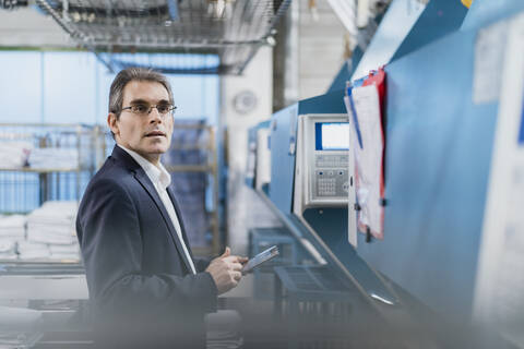 Älterer Geschäftsmann hält Tablet in einer Fabrik, lizenzfreies Stockfoto