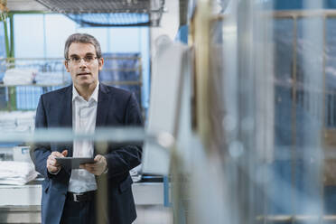 Portrait of a mature businessman holding tablet in a factory - DIGF10732