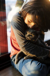 Boy cuddling cat at home - VABF02903