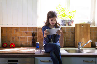 Mädchen sitzt am Waschbecken in der Küche und schaut auf ein digitales Tablet - LVF08876