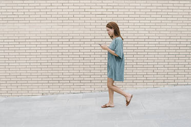 Woman using smartphone while walking in the street - XLGF00161