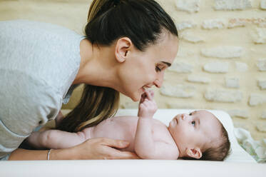 Baby girl touching lips of her mother, lying on changing table - KIJF03012