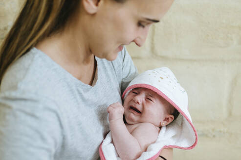 Mutter hält ihr weinendes Baby im Bademantel - KIJF03013