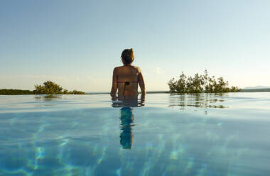 Back view of woman standing in infinity pool - VEGF02164