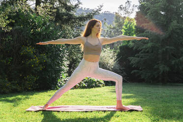 Junge Frau macht Yoga auf einer Matte im Gras - AFVF06258