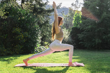 Young woman doing yoga on a mat in grass - AFVF06259