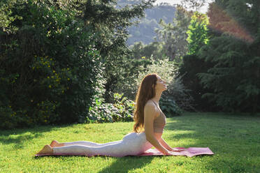 Young woman doing yoga on a mat in grass - AFVF06260