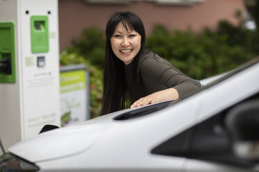 Carsharing, lächelnde Frau beim Aufladen eines Elektroautos - SGF02638