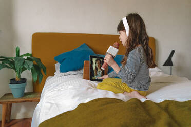 Mädchen singt mit Mikro und benutzt Tablet für ein Video auf dem Bett - ERRF03730