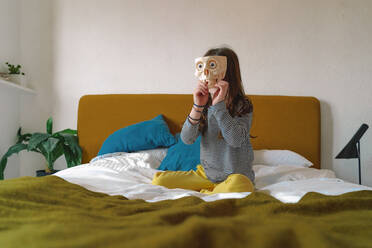 Mädchen spielt mit zahnlosem Schädel auf dem Bett sitzend zu Hause - ERRF03736