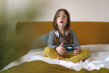 Girl playing video game sitting on bed - ERRF03737