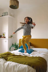 Girl jumping on bed and listening music with headphones - ERRF03740