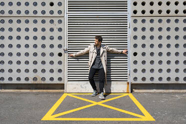 Mittlerer erwachsener Mann in gelb markiertem Bereich vor einer Betonwand stehend, mit ausgestreckten Armen - MAUF03404