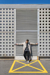 Mittlerer erwachsener Mann in gelb markiertem Bereich vor einer Betonwand stehend, mit ausgestreckten Armen - MAUF03405
