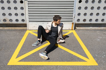 Helpless man sitting on ground in yellow marked area in front of concrete wall - MAUF03408