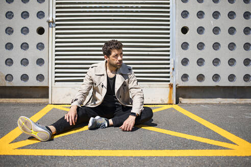 Hilfloser Mann sitzt auf dem Boden im gelb markierten Bereich vor einer Betonmauer - MAUF03409