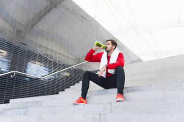 Junger Mann macht eine Pause vom Training und trinkt aus einer Flasche - DIGF10776