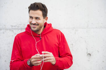 Portrait of sporty young man listening to music at a concrete wall - DIGF10782