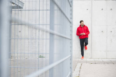 Sporty young man listening to music at a concrete wall - DIGF10783