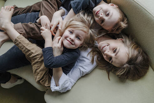 High angle view of happy mother lying with sons on sofa in living room at home - OGF00399