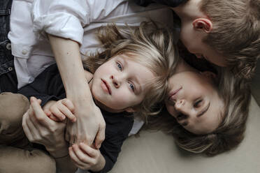 Directly above view of blond boy lying with brother and mother on sofa at home - OGF00400