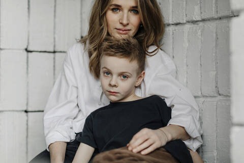 Portrait of confident mother with son sitting on niche at home stock photo