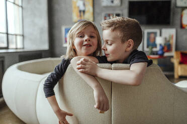 Portrait of smiling cute boy with brother on sofa in living room at home - OGF00410