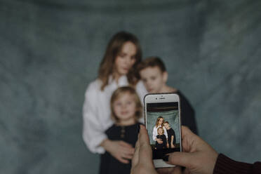 Hand einer Frau, die ihre Familie zu Hause mit dem Smartphone fotografiert - OGF00416