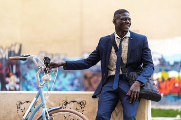 Smiling young businessman with bicycle in the city - EGAF00079