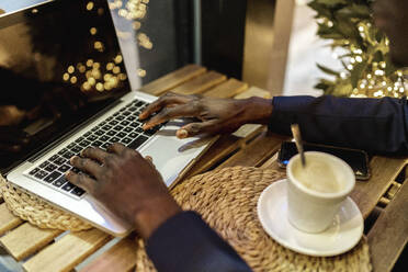 Crop view of young businessman working on laptop in a coffee shop - EGAF00085