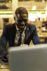 Lächelnder junger Geschäftsmann arbeitet an einem Laptop in einem Café - EGAF00086