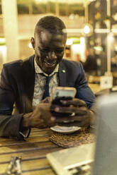 Smiling young businessman using smartphone in a coffee shop - EGAF00088