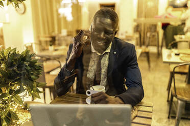 Porträt eines lächelnden Geschäftsmannes am Telefon in einem Kaffeehaus - EGAF00089