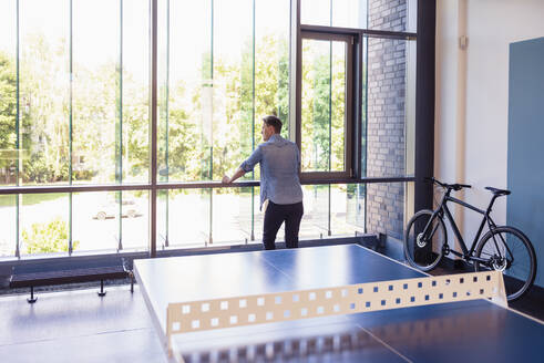 Geschäftsmann steht in einem Loft-Büro und schaut aus dem Fenster - DIGF10831