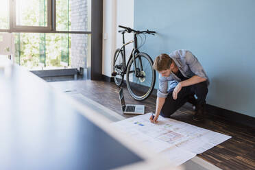 Casual businessman sitting on floor of loft office, working on a blueprint - DIGF10835