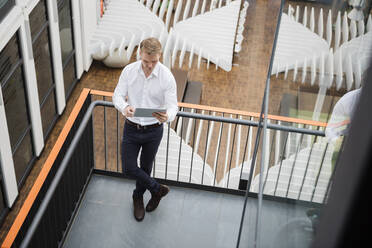 Businessman standing on gallery of modern office, using digitaö tablet - DIGF10836