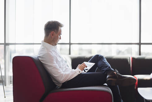 Geschäftsmann sitzt auf der Couch modernen Büro, mit digitalen Tablet - DIGF10838