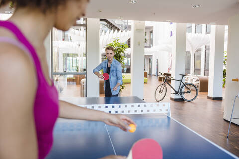 Junge Geschäftsleute spielen Tischtennis im Loftbüro, lizenzfreies Stockfoto