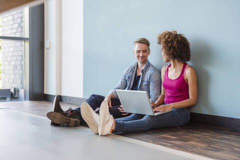 Junge Frau und Mann sitzen in einem modernen Büro auf dem Boden und benutzen einen Laptop, lizenzfreies Stockfoto