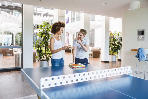 Junge Geschäftsleute essen gemeinsam Pizza zum Mittagessen in einem modernen Büro mit Tischtennisplatte - DIGF10865