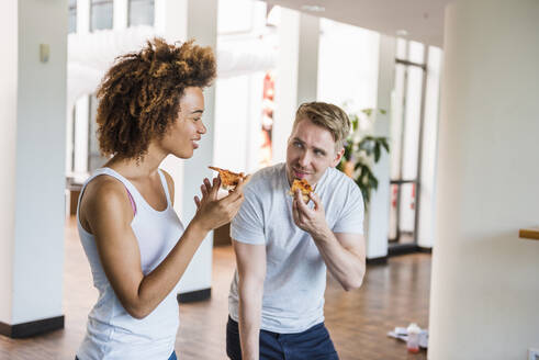 Junge Geschäftsleute essen gemeinsam Pizza zum Mittagessen in einem modernen Büro mit Tischtennisplatte - DIGF10866