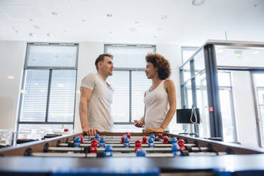 Junger Mann und Frau unterhalten sich in einem Büro mit einem Fußballtisch - DIGF10871