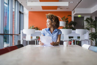 Young woman sitting in modern office, reading papers - DIGF10894