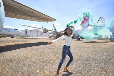 Cheerful young woman dancing with distress flare at airport runway on sunny day - VEGF02181