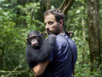 Kamerun, Pongo-Songo, Mann trägt Schimpanse (Pan troglodytes) im Wald - VEGF02203
