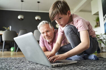 Vater und Sohn liegen auf dem Boden und arbeiten am Laptop - AUF00486