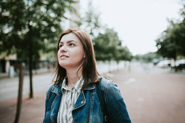 Germany, Berlin, Portrait of young brunette standing on sidewalk and looking up - VBF00032