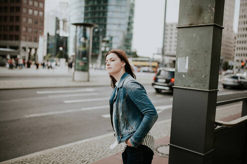 Deutschland, Berlin, Porträt einer jungen Frau, die auf dem Bürgersteig wartet - VBF00041